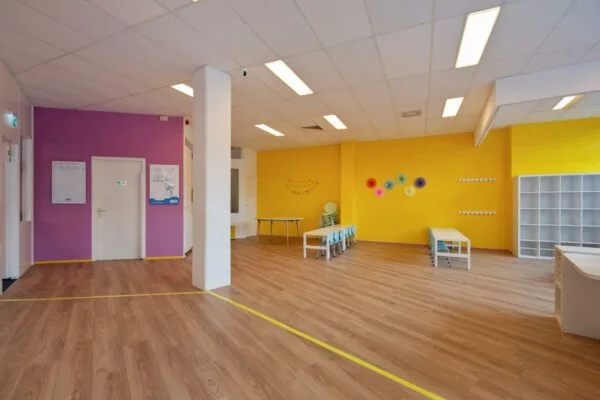 Kleurrijk en ruim lokaal in een kinderdagverblijf aan de Koningin Julianalaan met tafels, stoelen en vrolijke wanddecoratie.